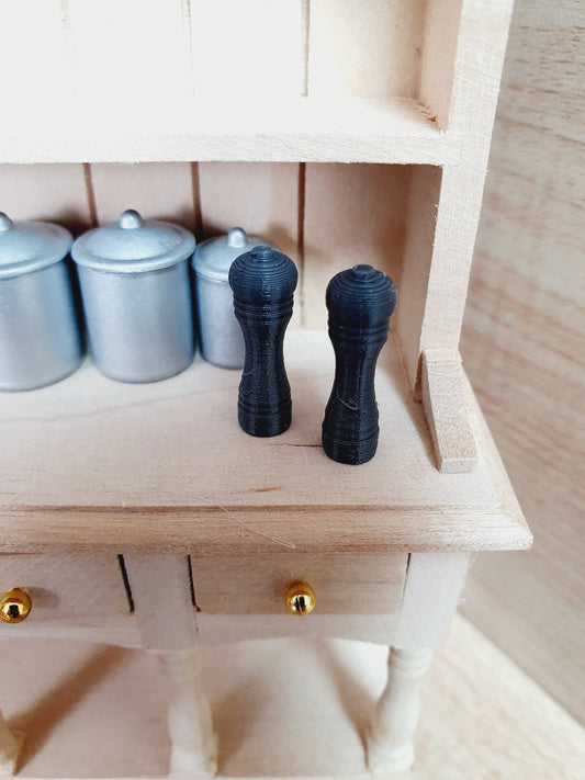 May include: Two black salt and pepper shakers on a wooden shelf with three silver canisters behind them.