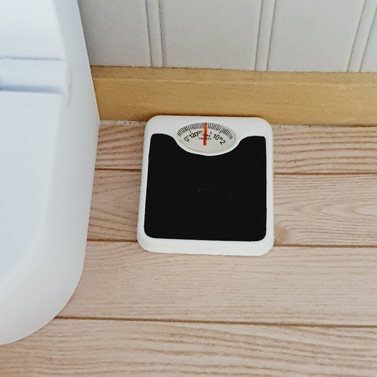 Black and white 1:12 scale dolls house bathroom scales with a dial, beside a white toilet on a wooden floor