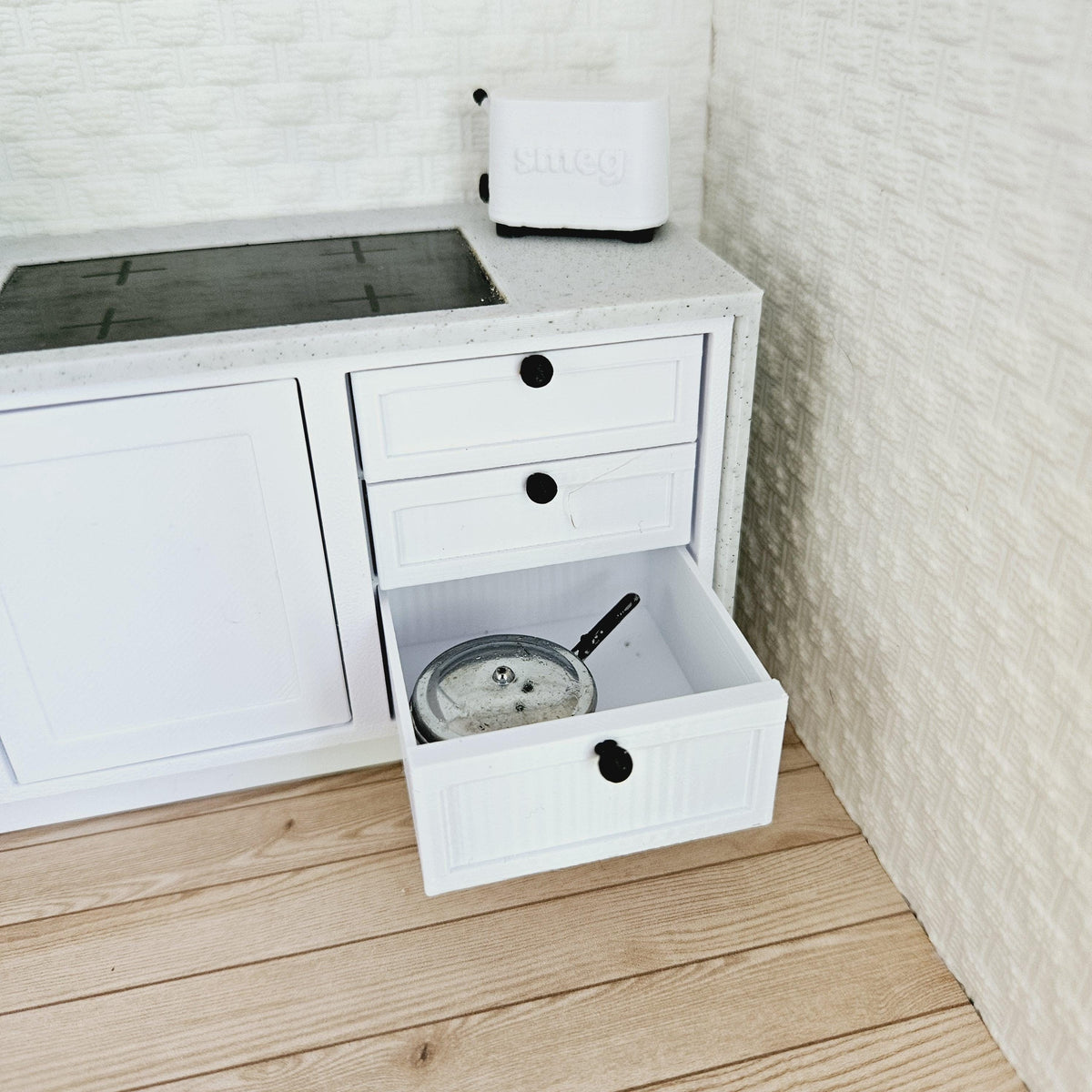dollhouse modern kitchen unit, 3 white cupboards with 1 shelf inside, 3 white drawers, wood effect cutlery tray, black knob handles, grey waterfall worktop, black sink and tap, black induction hob, 3d printed, 12th scale miniature