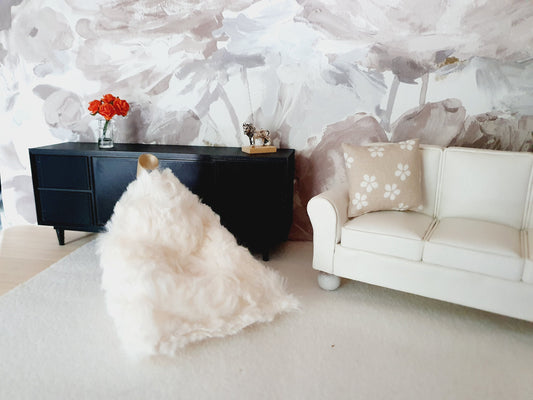 May include: A white faux fur bean bag chair sits on a white rug in a living room. A white sofa with a beige cushion featuring white flowers is in the background. A black cabinet with a small metal sculpture of a bull sits on top of the cabinet.