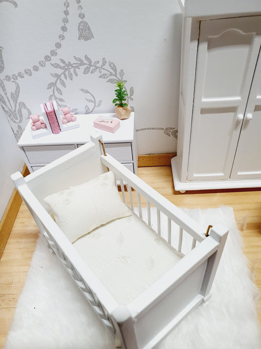 May include: White wooden cot with a white mattress and a white pillow with embroidered details. The cot is set on a white fluffy rug.