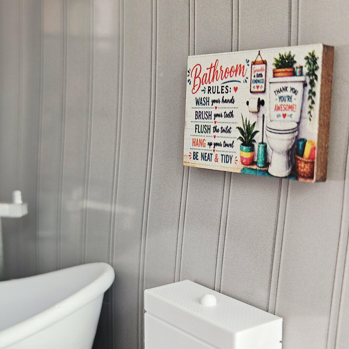 May include: A rectangular wooden sign with the words "Bathroom Rules" in red script. The sign includes instructions like "Wash your hands" and "Brush your teeth", along with a picture of a toilet and plants. The sign is mounted on a grey wall.