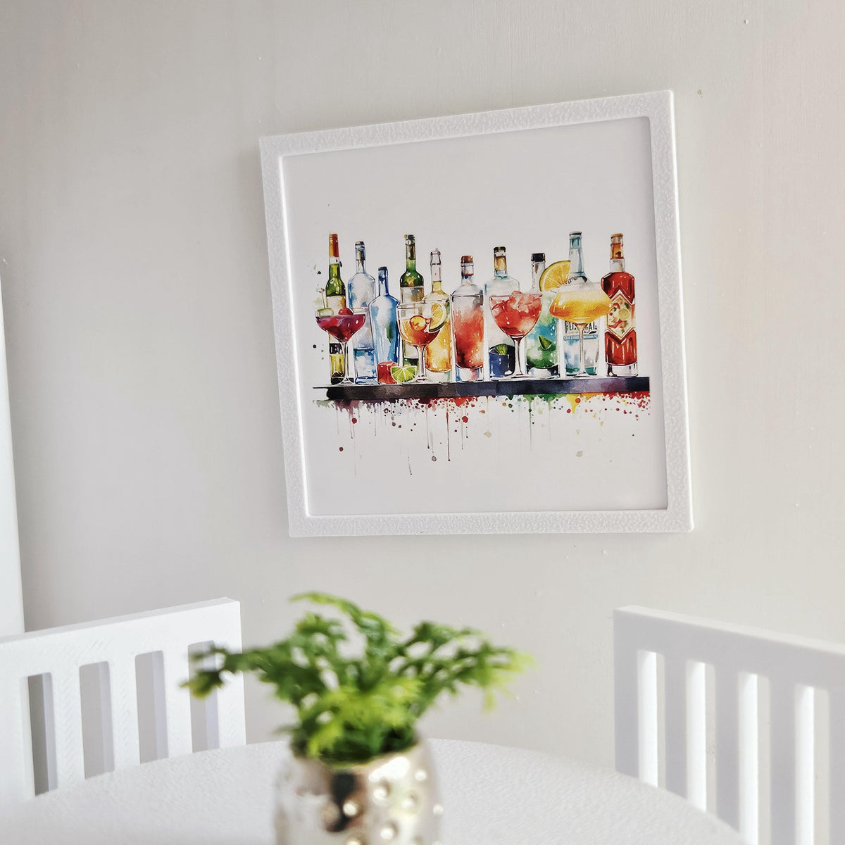 May include: A framed watercolour print depicting a selection of cocktail bottles and glasses. The artwork displays a range of alcoholic drinks in vivid colours, set against a white backdrop, and enclosed in a white frame.