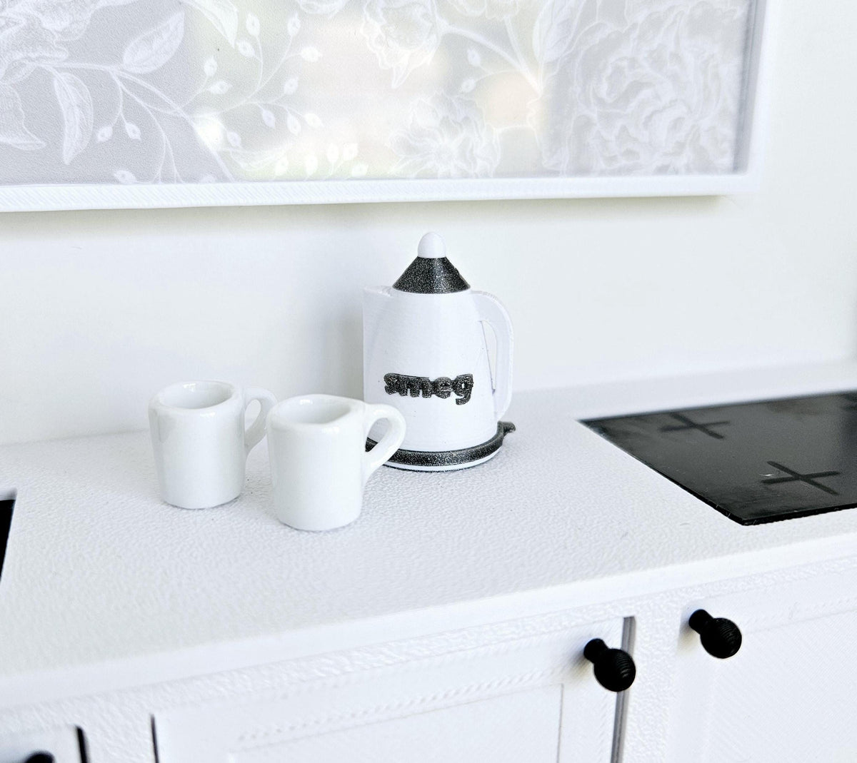 May include: White ceramic mugs and a white kettle with a black Smeg logo on a white worktop. The worktop has a black hob.