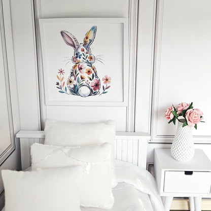 May include: A framed watercolour print of a rabbit adorned with colourful flowers. The artwork is displayed above a bed with white pillows and bedding. A white vase with pink flowers sits on a bedside table.