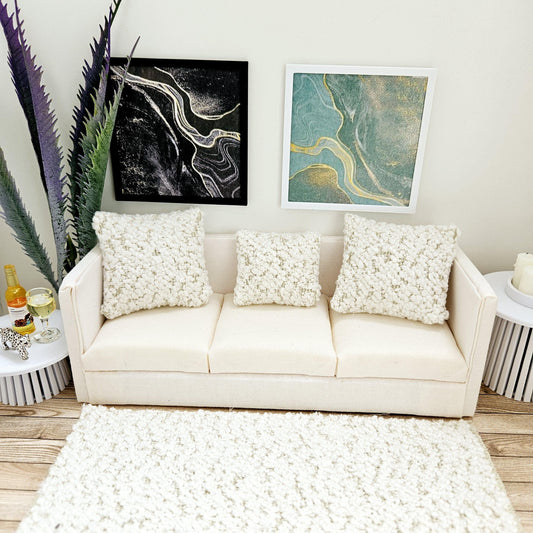 May include: A white sofa with three white throw pillows, a white rug, and two abstract paintings on the wall. The sofa is in a living room setting.