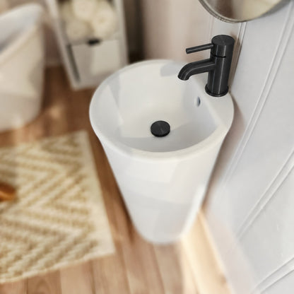 Close-up of white miniature round bathroom sink with black tap and matching black plug