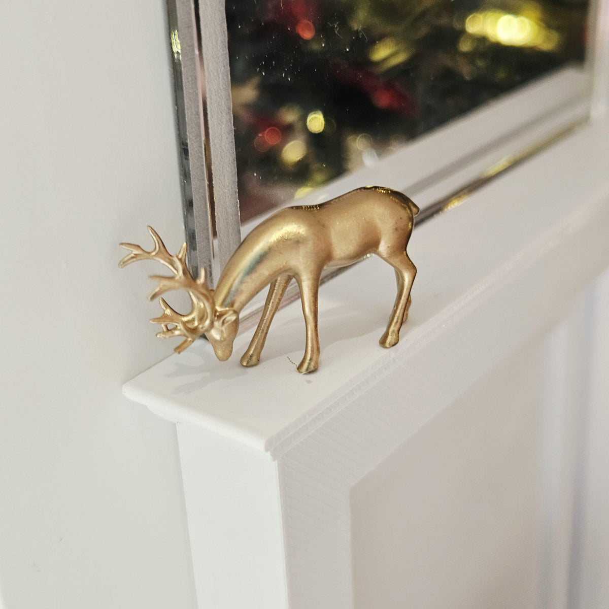 Gold Christmas reindeer ornament with lowered head and antlers on a dolls house mantelpiece, 1:12 scale