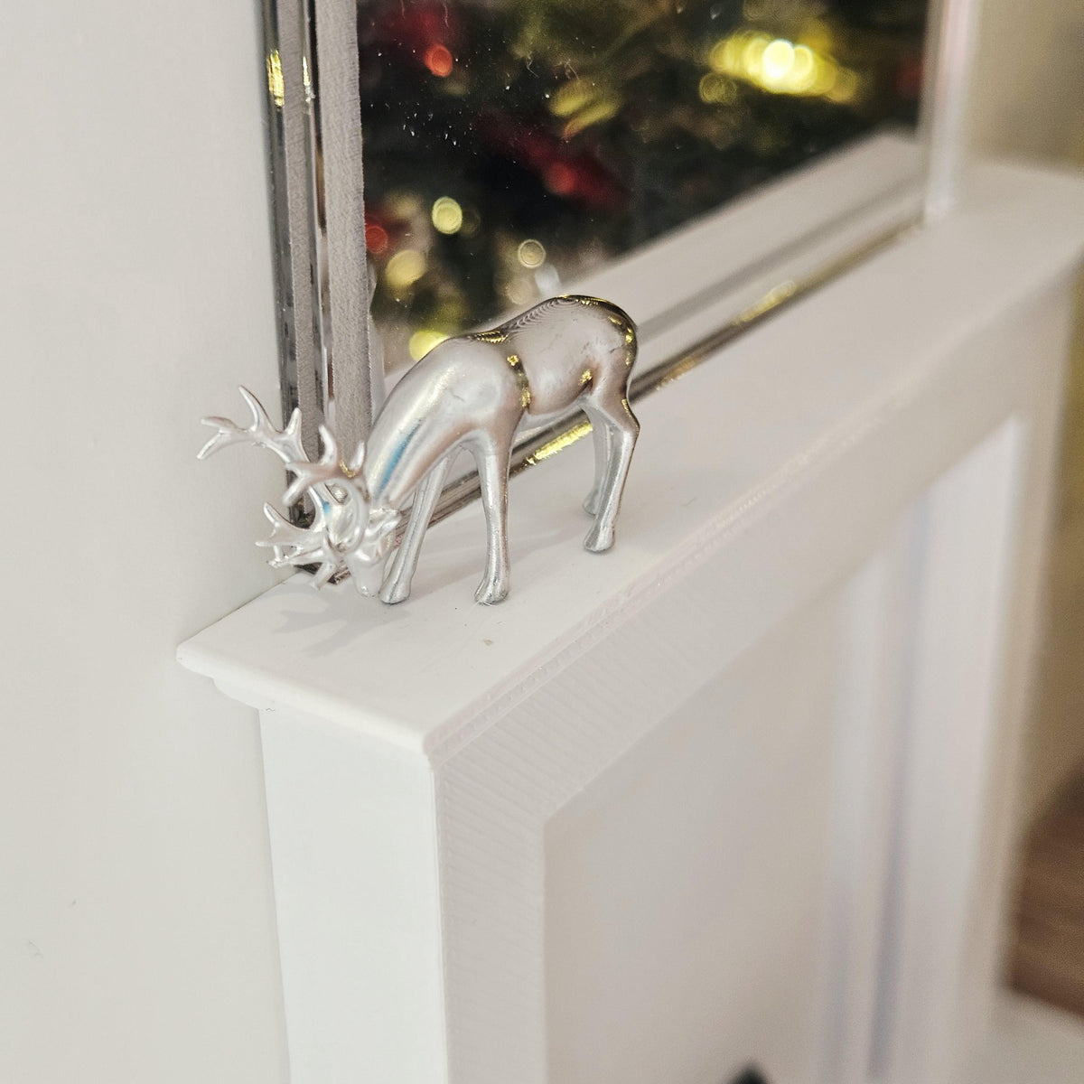 Silver Christmas reindeer ornament with lowered head and antlers on a dolls house mantelpiece, 1:12 scale