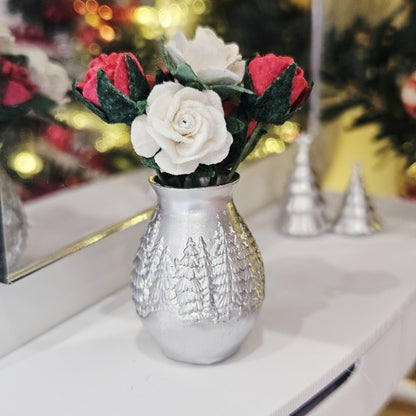 Silver Christmas vase showing raised fir tree decoration beneath red and white roses, with miniature silver trees in the background.