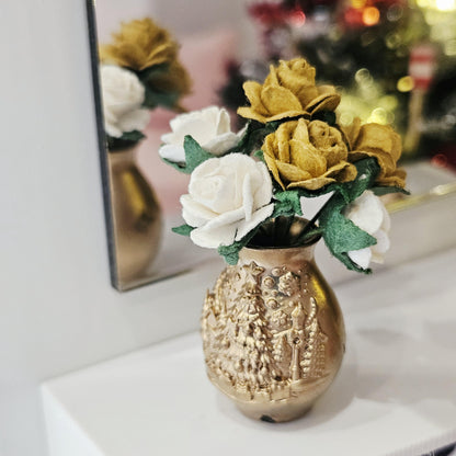 Angled view of gold and white roses in a gold-coloured vase with raised Christmas tree decoration, reflected in a mirror.