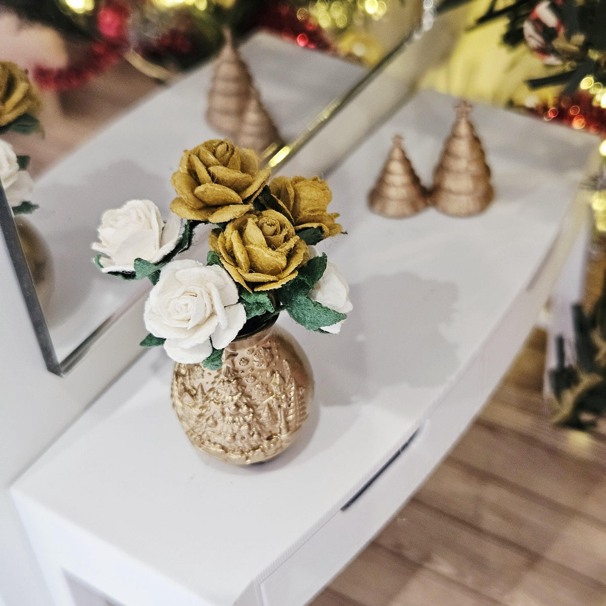 Elevated view of the gold-coloured vase and gold and white roses on a white sideboard, with miniature trees behind.