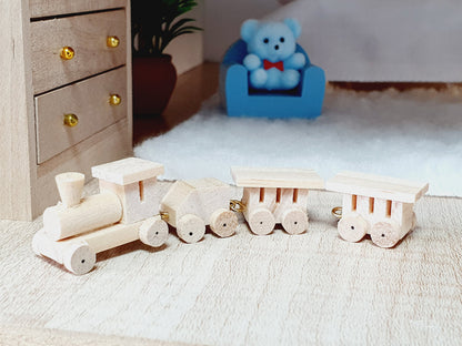 Pale wooden four-piece toy train viewed from the side on a miniature bedroom floor, with a chest of drawers and teddy bear behind.