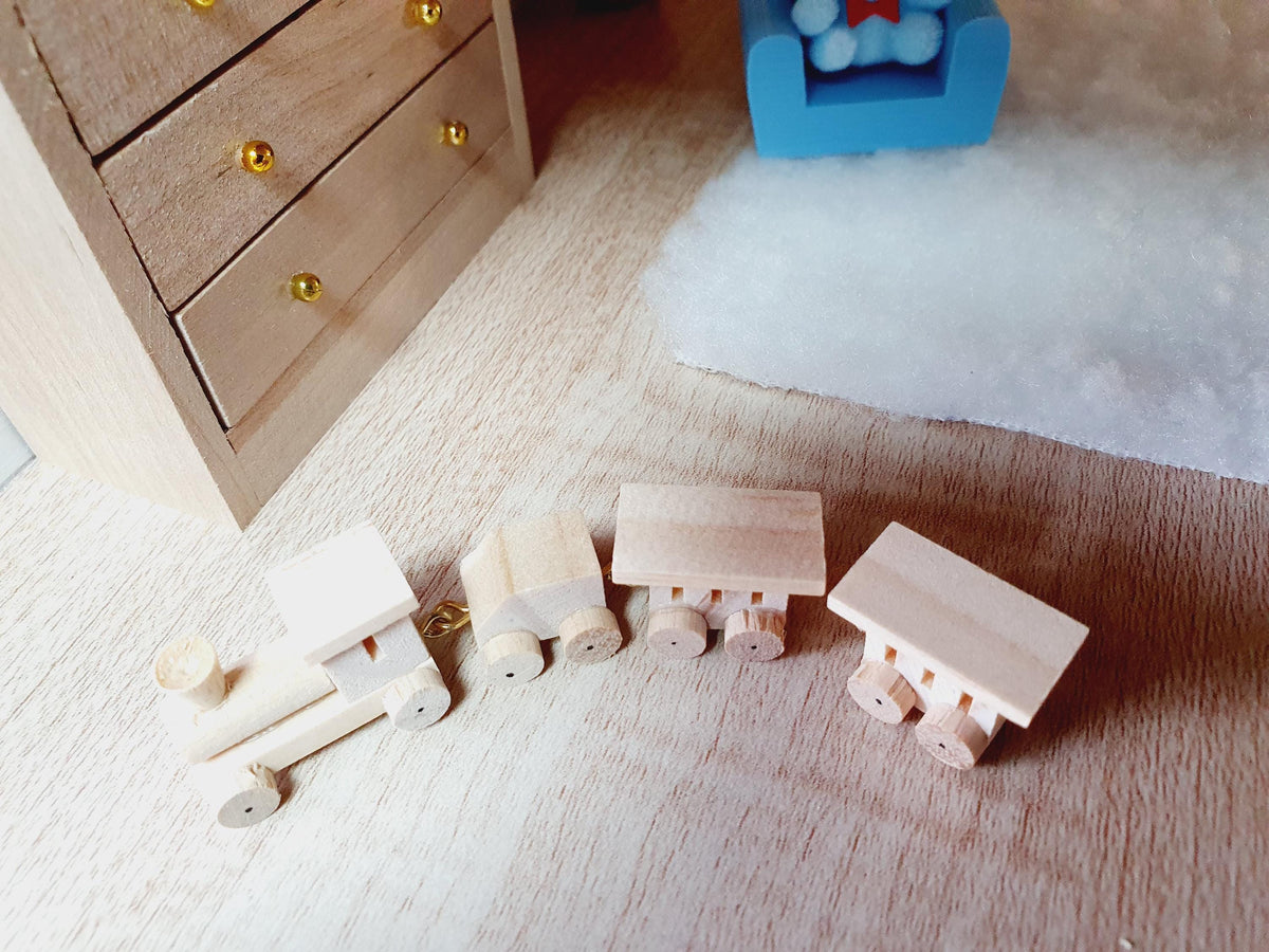 Four-piece wooden toy train viewed from above, showing the engine, small wagon and two roofed carriages beside a miniature bedroom rug.