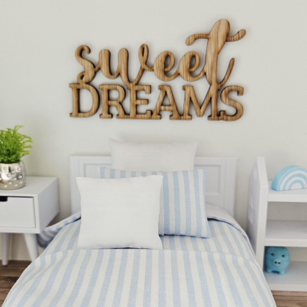 Sweet Dreams wooden sign above a white miniature bed with blue-striped bedding, flanked by a bedside table and shelving.