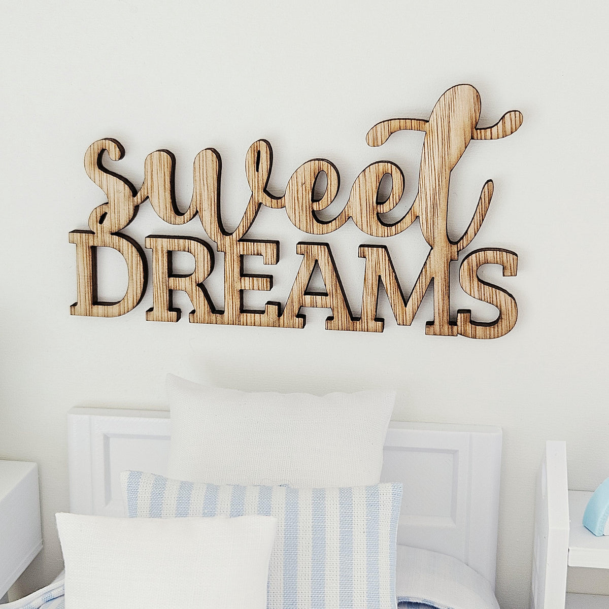 Front view of the Sweet Dreams sign, with flowing script above capital letters, displayed over a white miniature headboard.