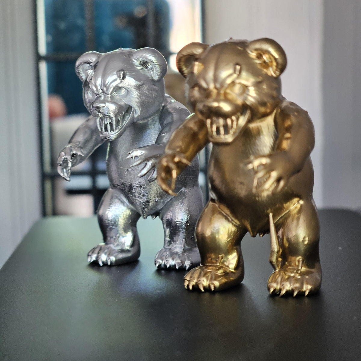 Gold and silver scary bear ornaments on a black tabletop, with the silver bear’s snarling face sharply visible.