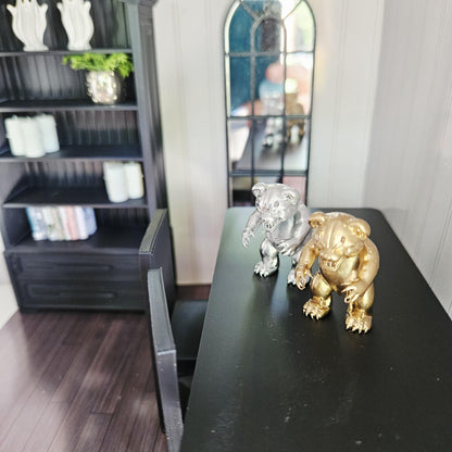 Elevated view of silver and gold scary bear ornaments on a black table in a miniature room with shelving and an arched mirror.