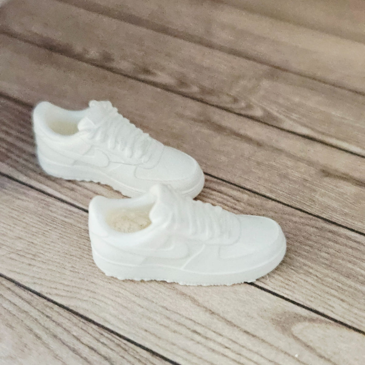 Actual pair of white miniature trainers on a wooden dolls house floor, side view