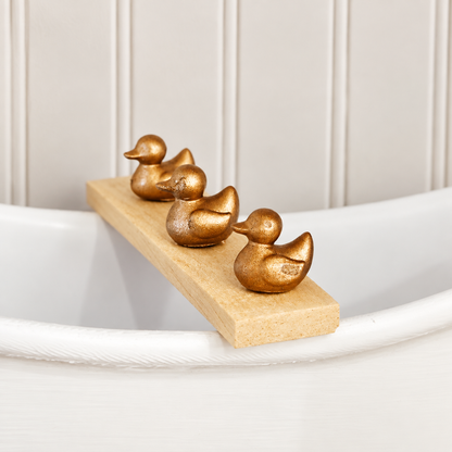 Side-angle view of three metallic ducks on a 1:12 scale wooden bath board